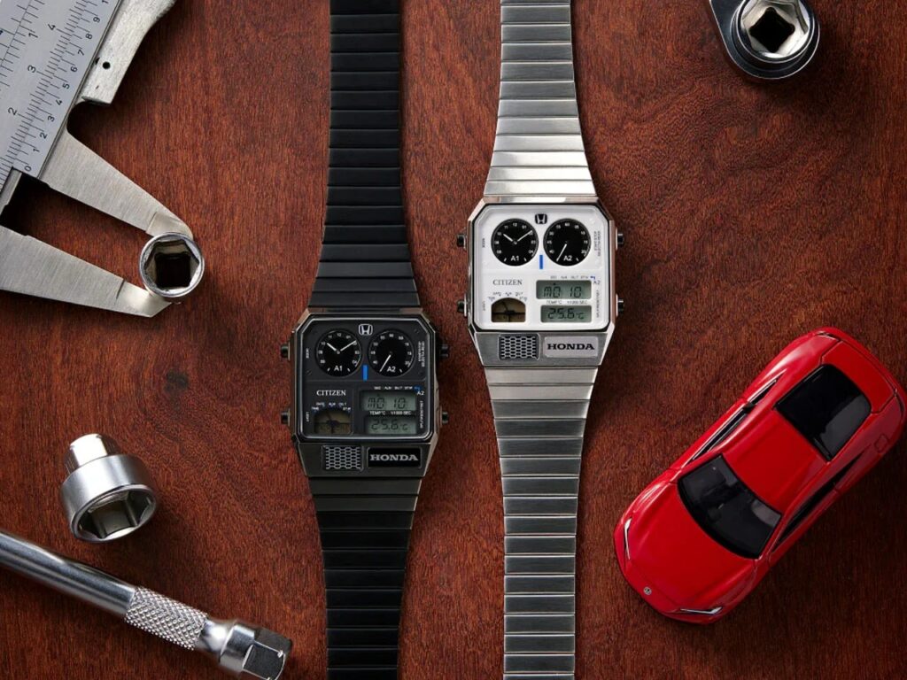 Black and silver Citizen Ana-Digi Temp watches on a wooden surface with a miniature red Honda car and mechanical tools.