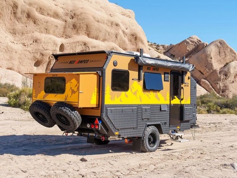 Yellow and black Terra 700 camper trailer parked in a desert area with its rear expansion deployed.