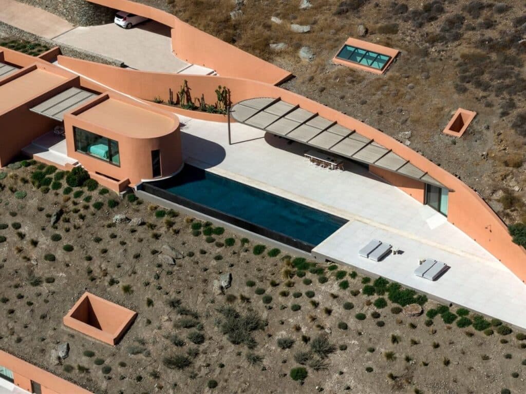 High-angle aerial view of the Oline resort terrace, featuring a long infinity pool, curved retaining walls, and minimalist outdoor furniture.
