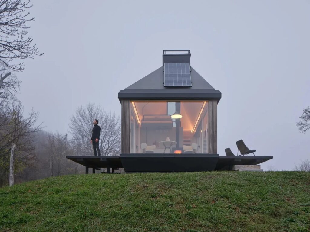 Evening view of Devin Cabin with interior lights glowing, a person standing on the deck under a foggy sky.