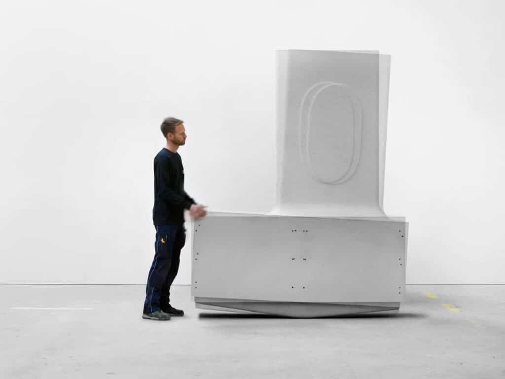 A person manually pushing a large L-shaped concrete modular component of the Heirloom House project.