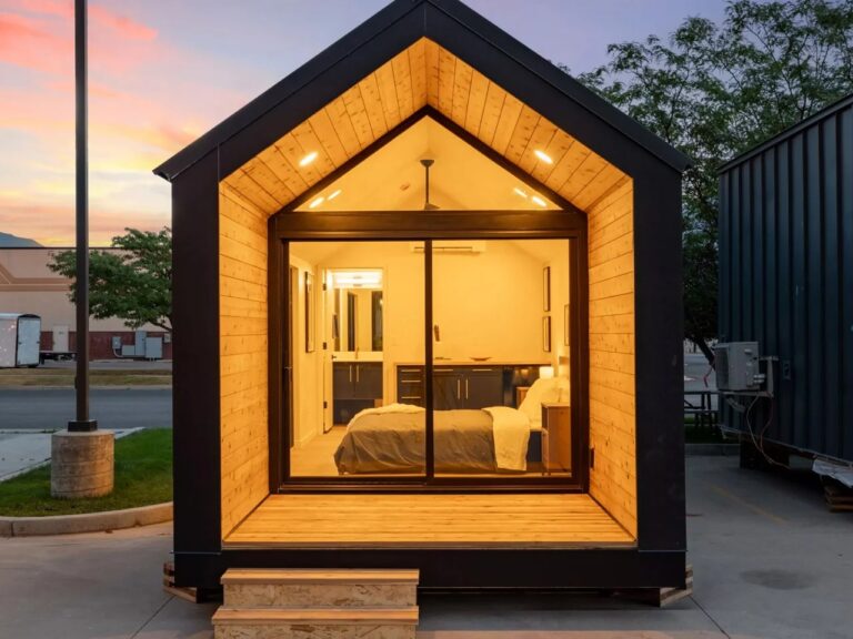 Front view of Mysa 200 tiny home with warm wood-cladded gabled entrance and glass sliding doors at sunset.