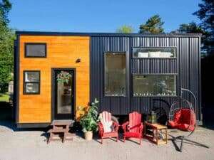 Exterior of Premium Vista tiny house featuring black corrugated metal siding and warm cedar wood accents with outdoor seating.
