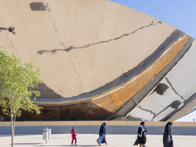 Pedestrians walking past the large mirrored exterior wall of Qasr Al-Hukm station, reflecting the surrounding plaza.