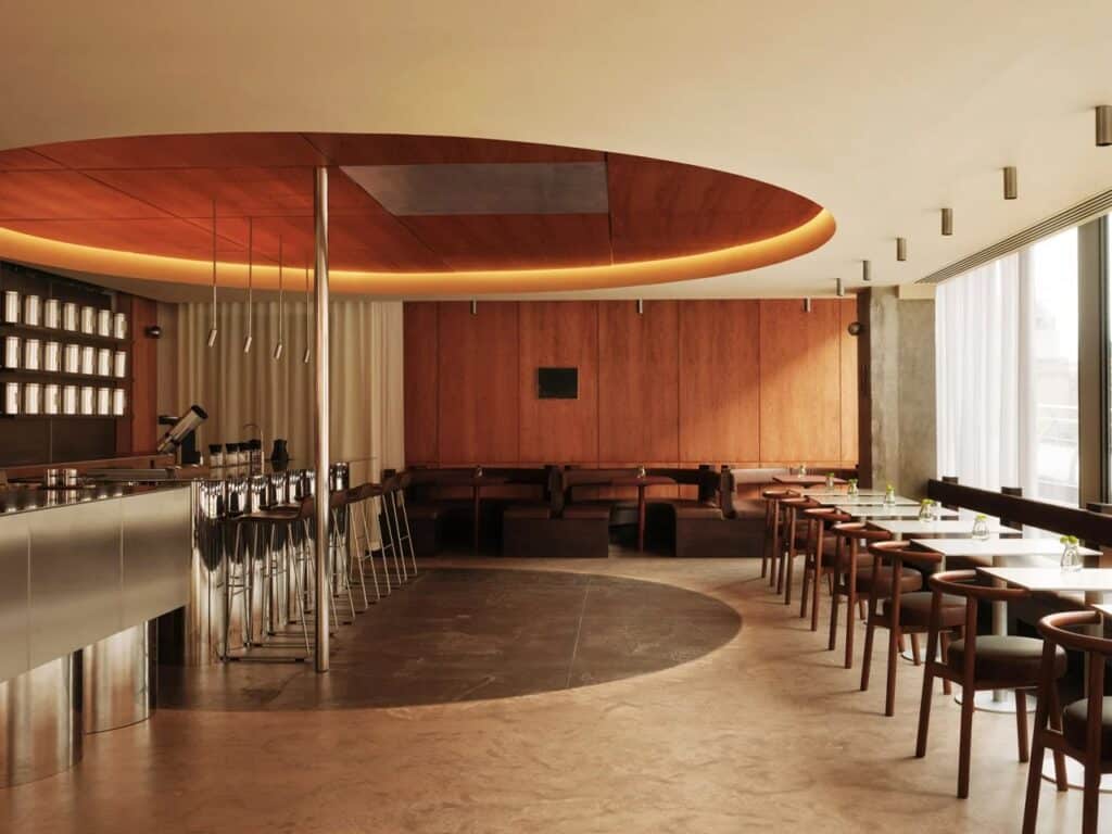 Modern interior of WatchHouse cafe featuring a circular ceiling void and industrial metal coffee bar.