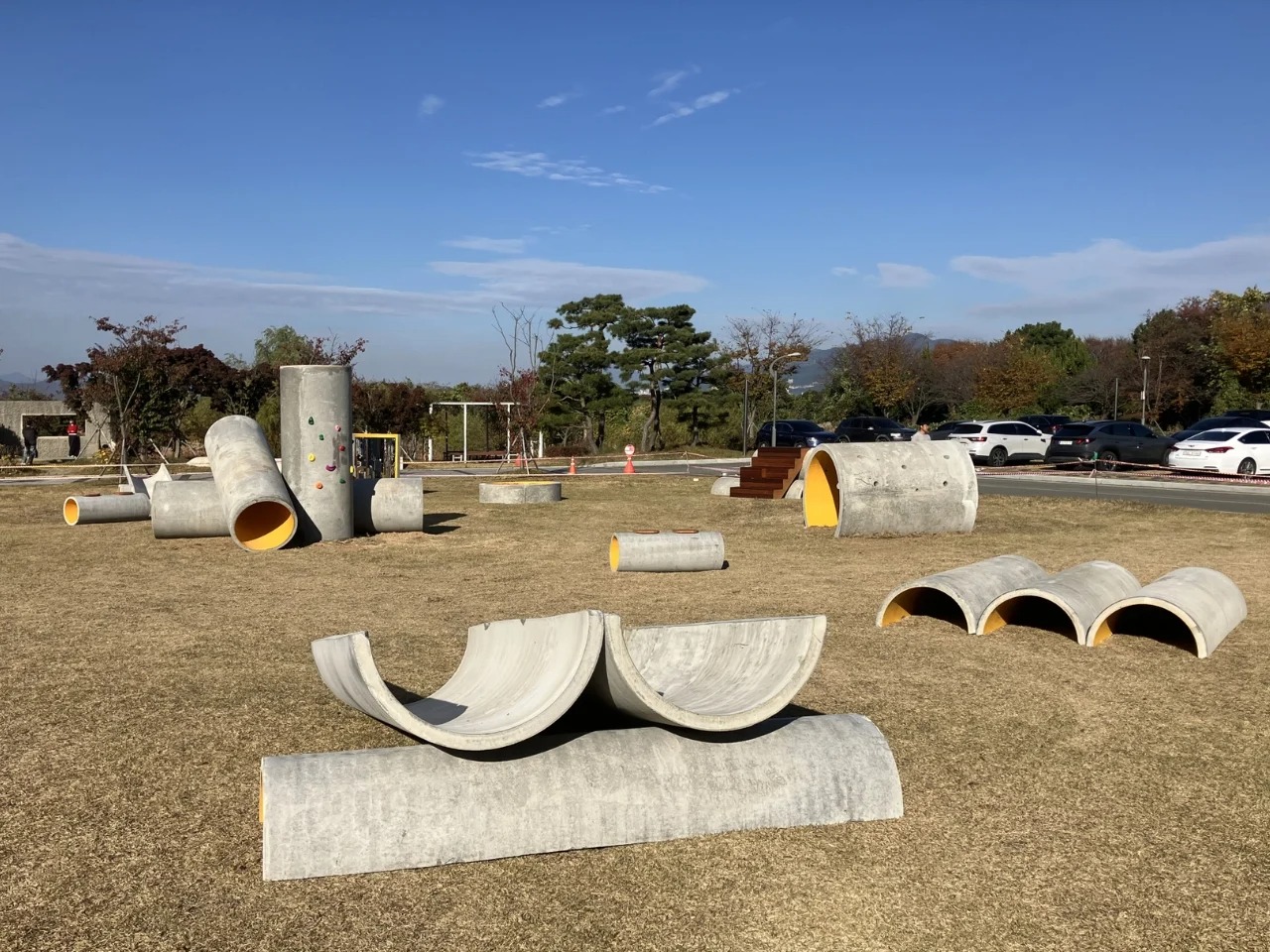 Scattered concrete pipes of various sizes in an open field as part of the Concrete Utopia installation at Busan Museum of Contemporary Art.