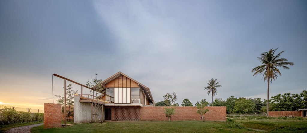 Wide shot of Baan SudSaenSuk at dusk showing the 45-degree rotation relative to the site boundaries and brick walls.