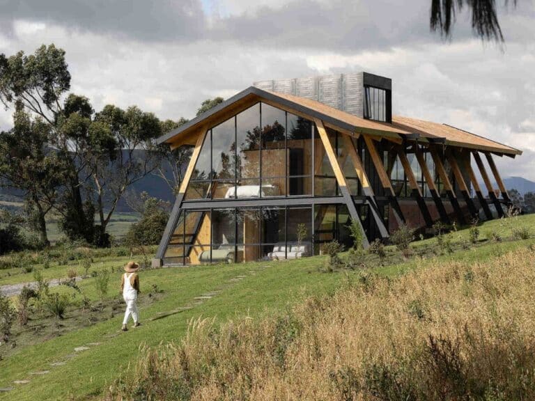 Exterior view of La Miradora house in Ecuador showing a gabled glass facade and timber structural ribs on a green sloping hill.