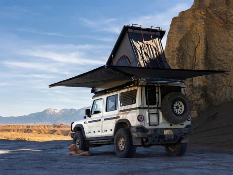 Side view of the Grand Bohemian 4x4 expedition vehicle with an expanded 270-degree awning and a rooftop pop-up tent in a desert landscape.