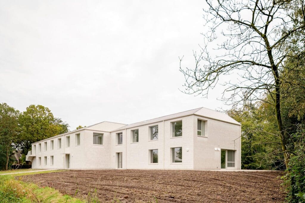 Wide perspective view of the Care Villa building, a two-story L-shaped structure with a white facade and pitched roofs in a rural setting.