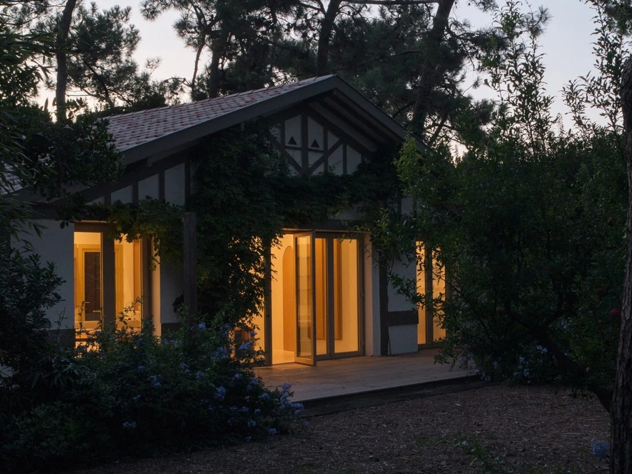 Exterior evening view of Seaside House showing glowing interior lights through glass doors nestled among pine trees.
