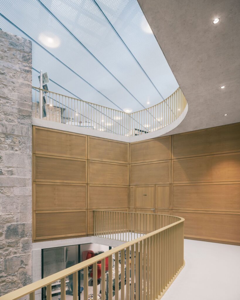Looking up through the atrium of La Manufacture Cultural Center featuring curved wooden balconies and a translucent ceiling.