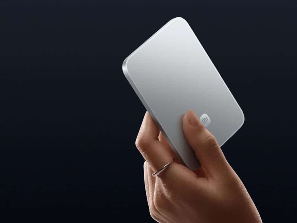 A close-up of a hand holding a silver ultra-slim power bank, showing its business-card-like thickness and ergonomic size.
