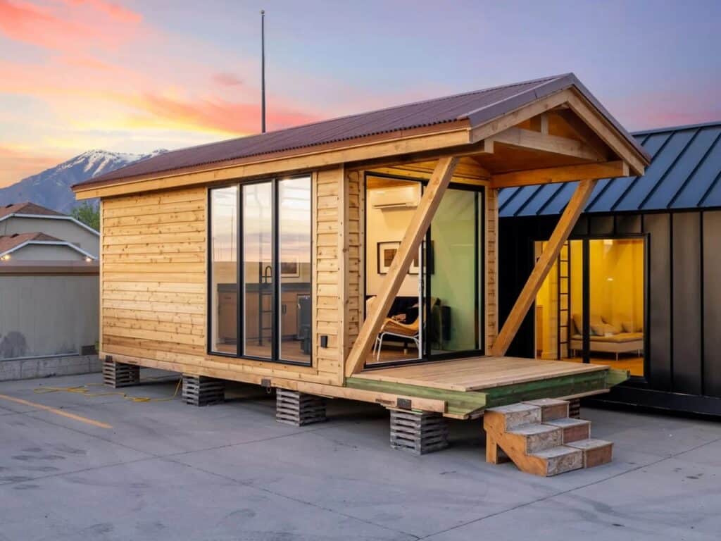 Angled exterior view of the Sledhaus 200 cabin with the front porch and mountains in the background.