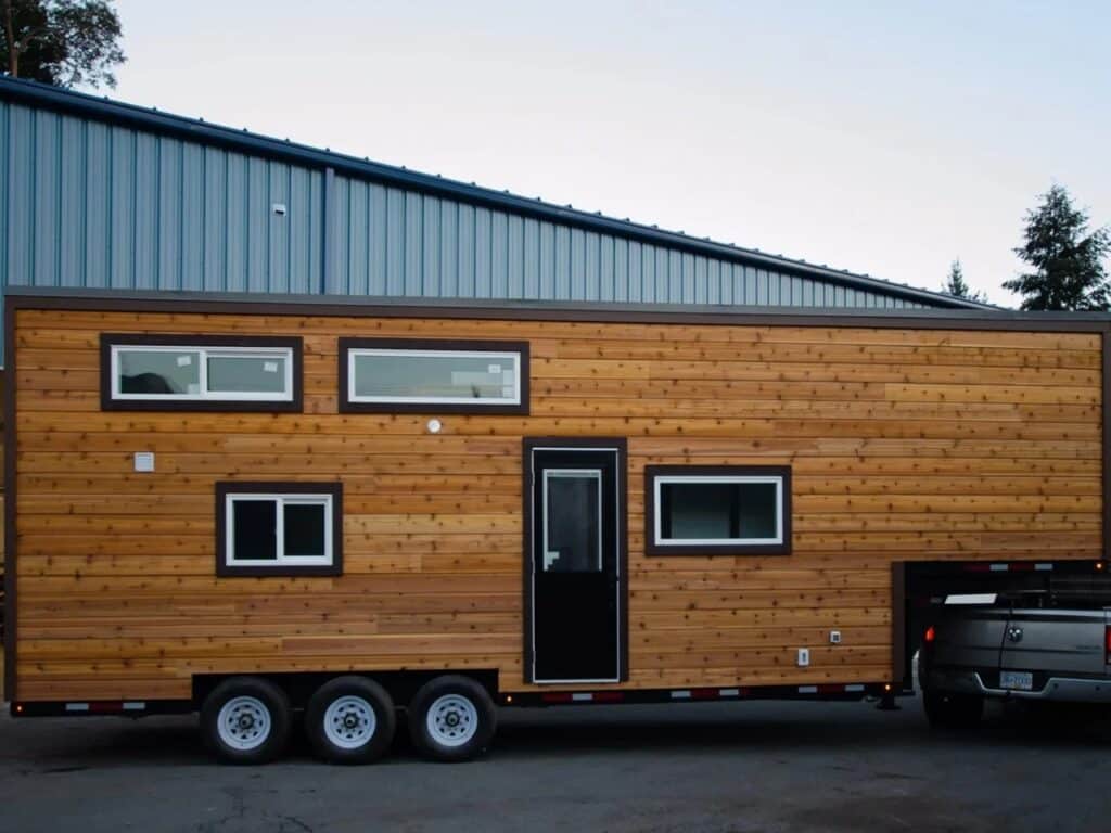Exterior side view of the Starling tiny home featuring natural wood siding and a triple-axle trailer base.