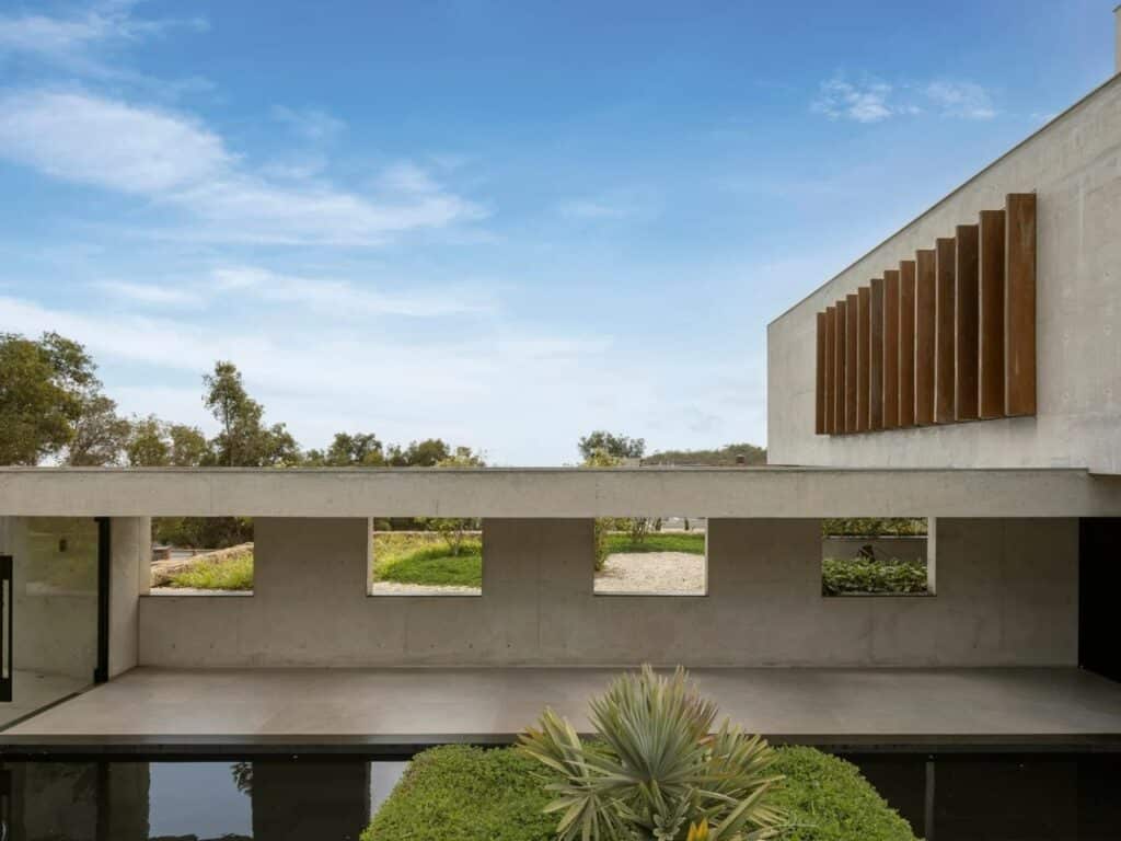 Reflective water pool at the entrance of GM House with vertical wooden louvers and concrete openings.