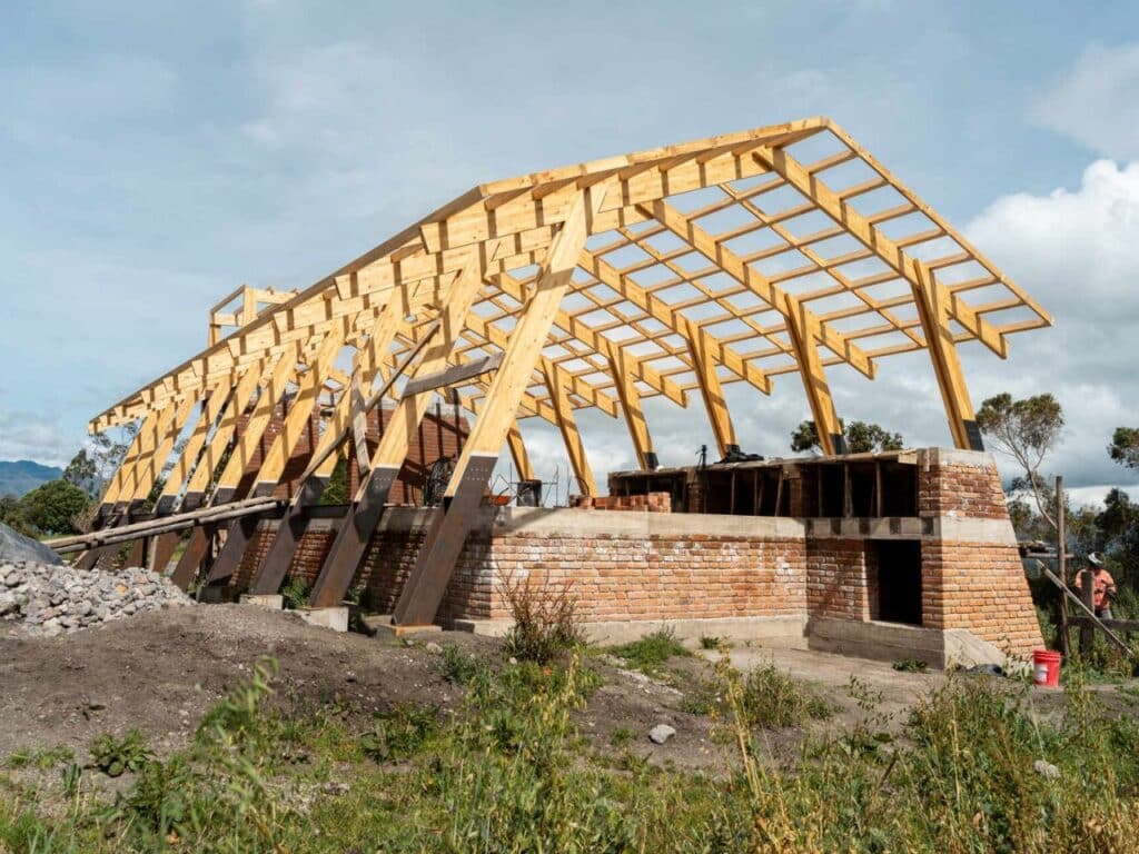 Construction phase of La Miradora house showing the wooden rib skeleton and brick foundation on a sloped site.