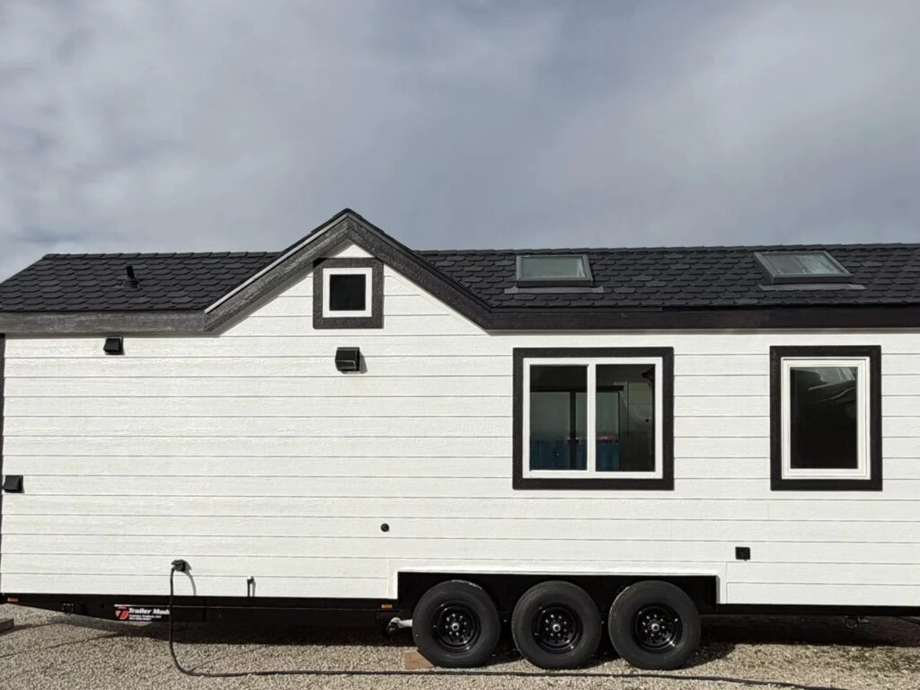 Side elevation of the Betty tiny house featuring white lap siding, black roof shingles, and skylights.