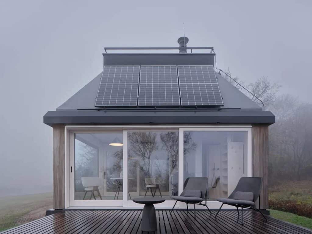 Frontal view of the Devin Cabin's glass facade and wooden deck with outdoor chairs in misty weather.