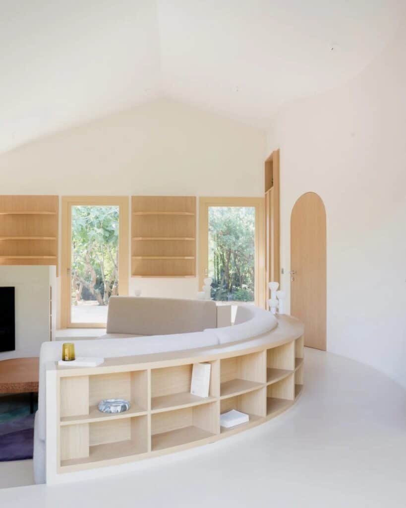 Interior of Seaside House featuring a curved wooden bookshelf wrapping around a central conversation pit with garden views.