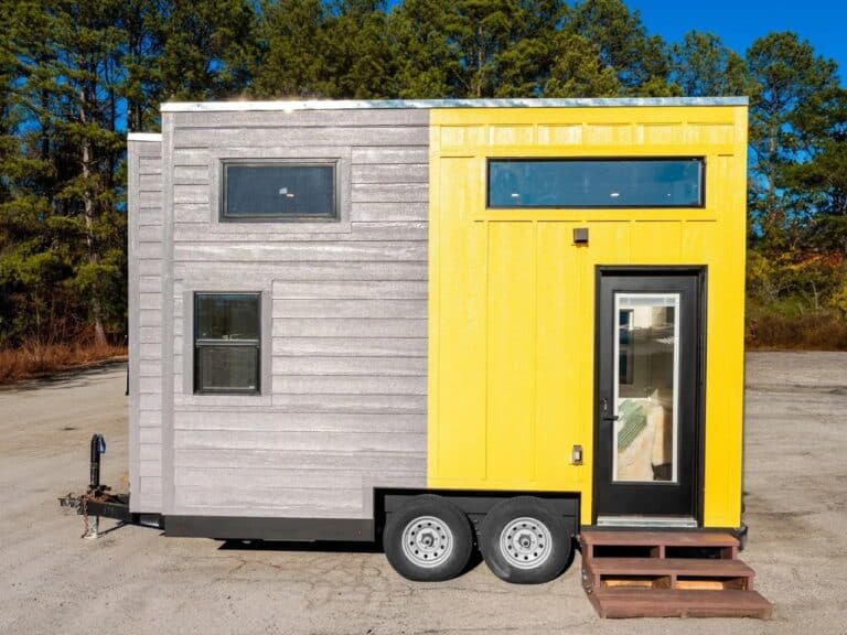 Side view of the Genesis 16 tiny house on a dual-axle trailer featuring a two-tone grey and yellow exterior cladding.