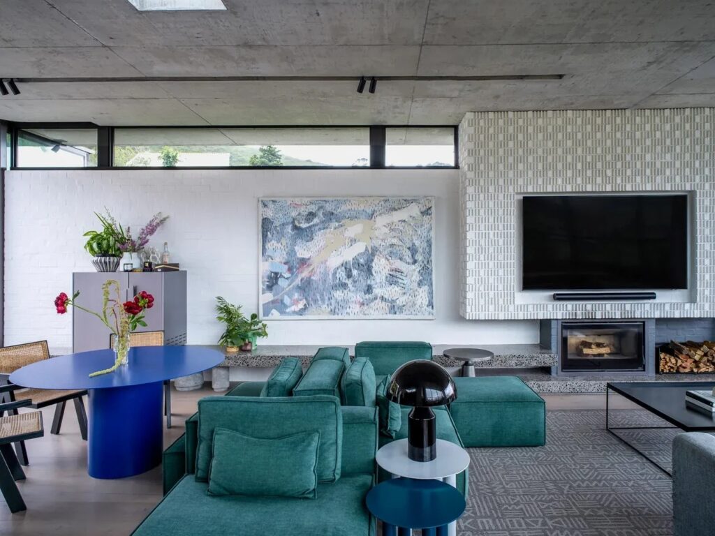 Modern living room interior with a teal sectional sofa, a textured white fireplace wall, and a large television.