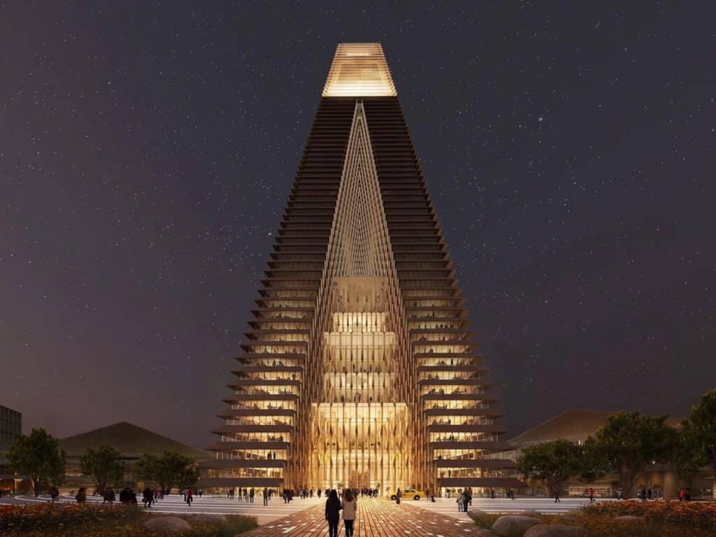 Frontal night view of the Alatau Iconic Complex pyramid tower with illuminated glass facades and a crowded public plaza in the Gateway District.