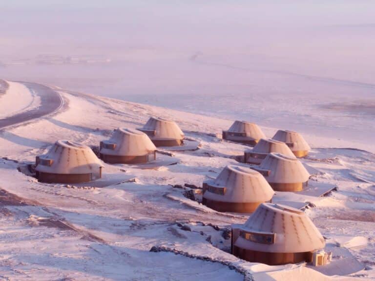 Aerial view of a cluster of volcanic-inspired architectural cabins in the snowy Inner Mongolia steppe at sunset.