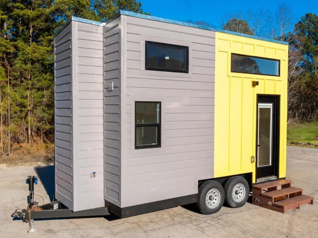 Perspective view of the Genesis 16 tiny home exterior showing the entrance door and wooden steps.