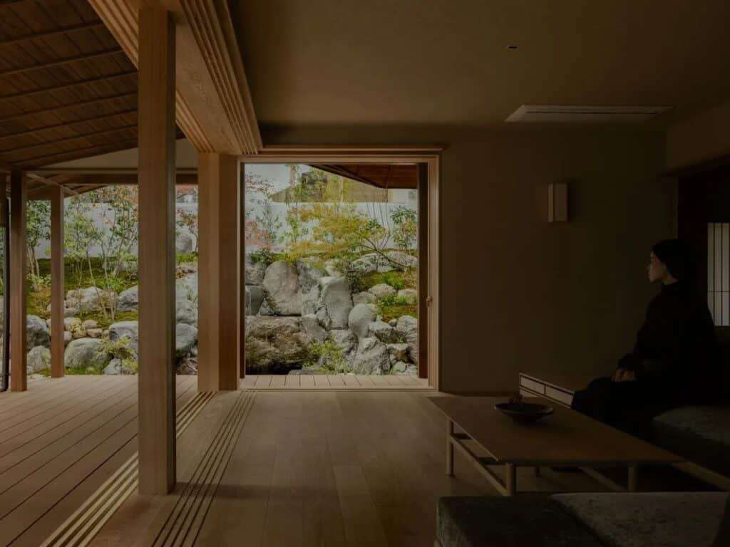 Low-angle interior shot of a minimalist living space with wooden beams and a large glass door facing a rock garden.