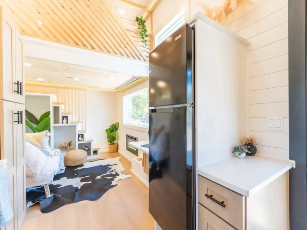 Perspective from the kitchen toward the living area of Premium Vista tiny house featuring a black refrigerator and storage cabinets.