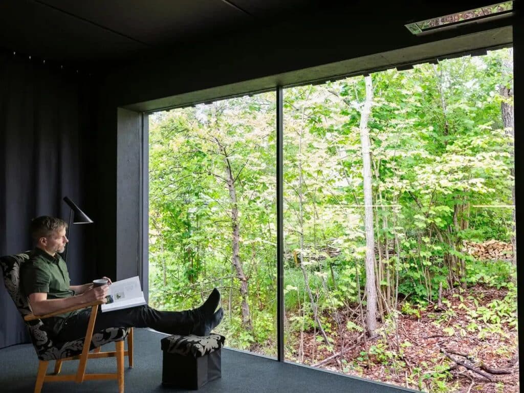 Resident sitting in a minimalist living area of Tiny House Shadow looking out through a large panoramic window.