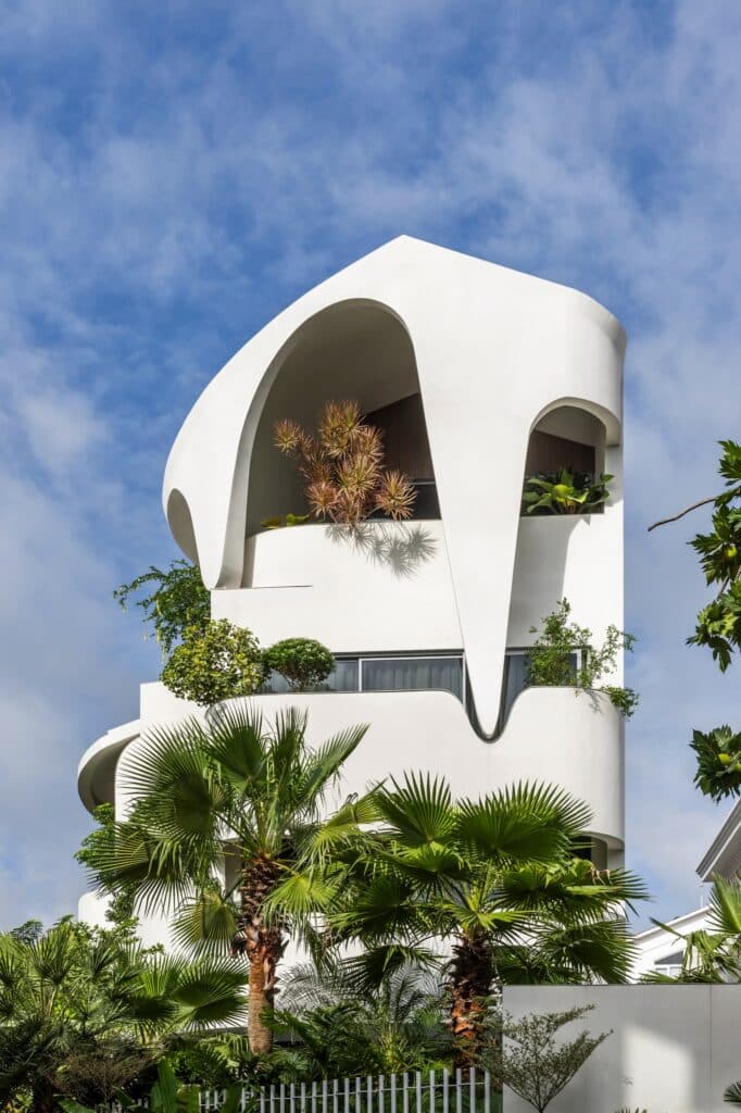 Vertical view of the white sculptural building against a blue sky, featuring teardrop-shaped architectural elements and palm trees.