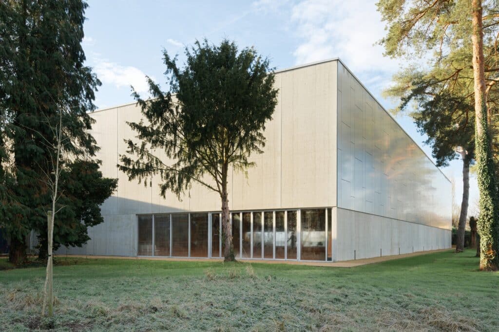 The corner of the Sporting Vichy building showcasing the transition between concrete walls and metallic cladding, framed by mature pine trees.