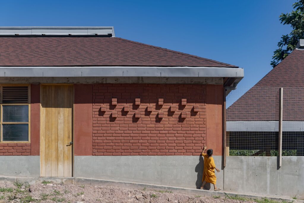 Close-up of a handmade clay brick wall with decorative protrusions and a wooden door at Sonomoro School.