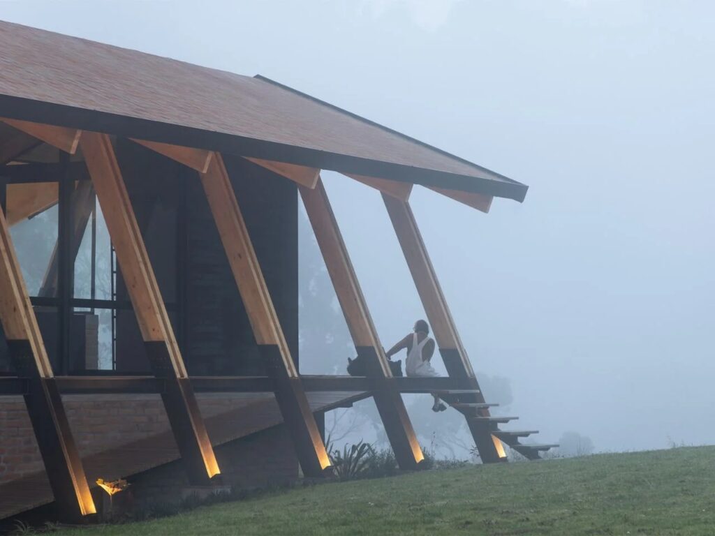 A person sitting on the edge of a wooden deck of La Miradora house overlooking a misty mountain landscape.
