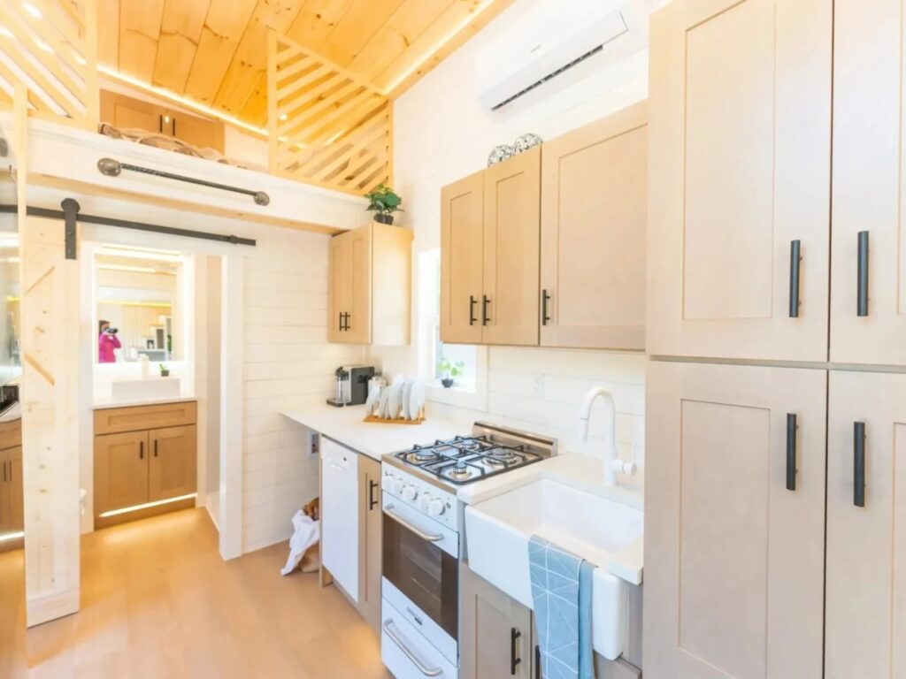 Close-up of a tiny house kitchen with a four-burner gas stove, white farmhouse sink, and quartz surfaces.