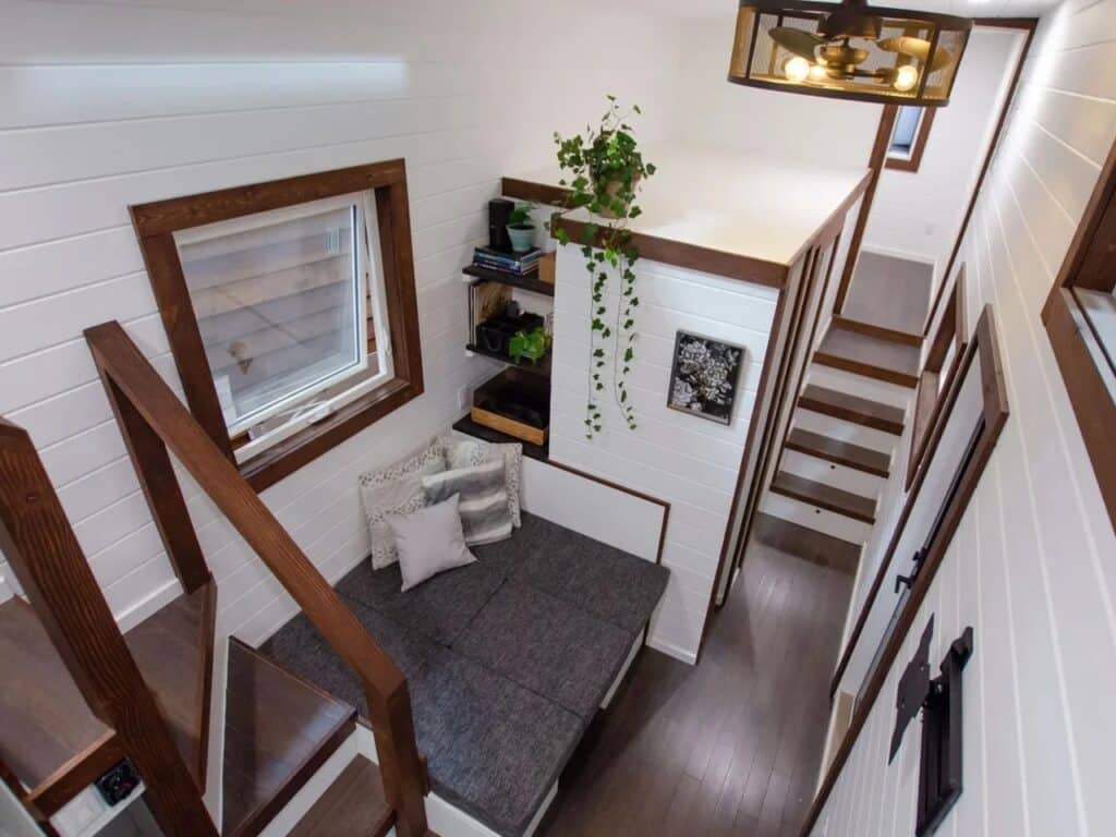 Interior high-angle view of a tiny home living area with a convertible gray sofa and white shiplap walls.