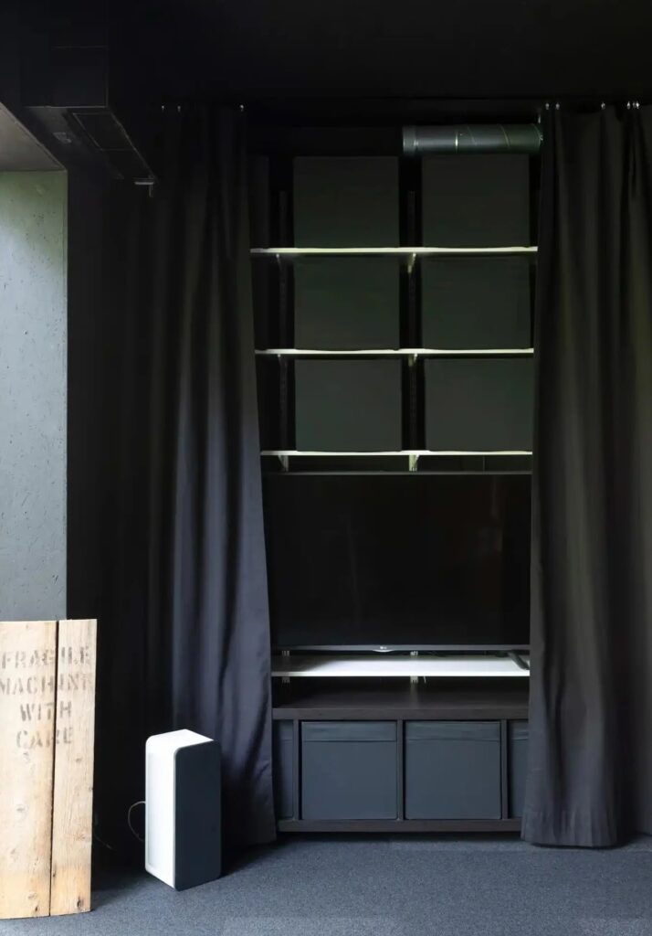 Flexible interior storage and media unit in Tiny House Shadow using heavy black curtains for spatial division.
