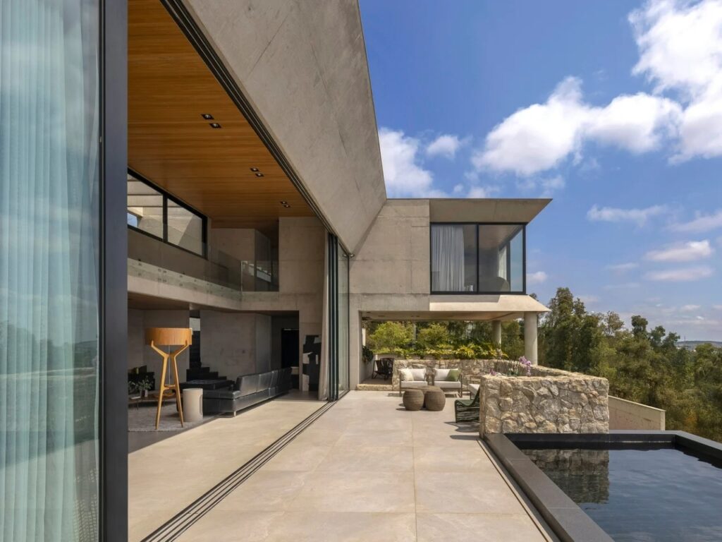 Large outdoor terrace of GM House with a dark swimming pool and open-plan living room view.