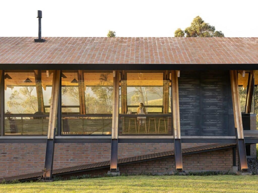 Side elevation of La Miradora house featuring a brick wall, glass windows, and an external wooden ramp.