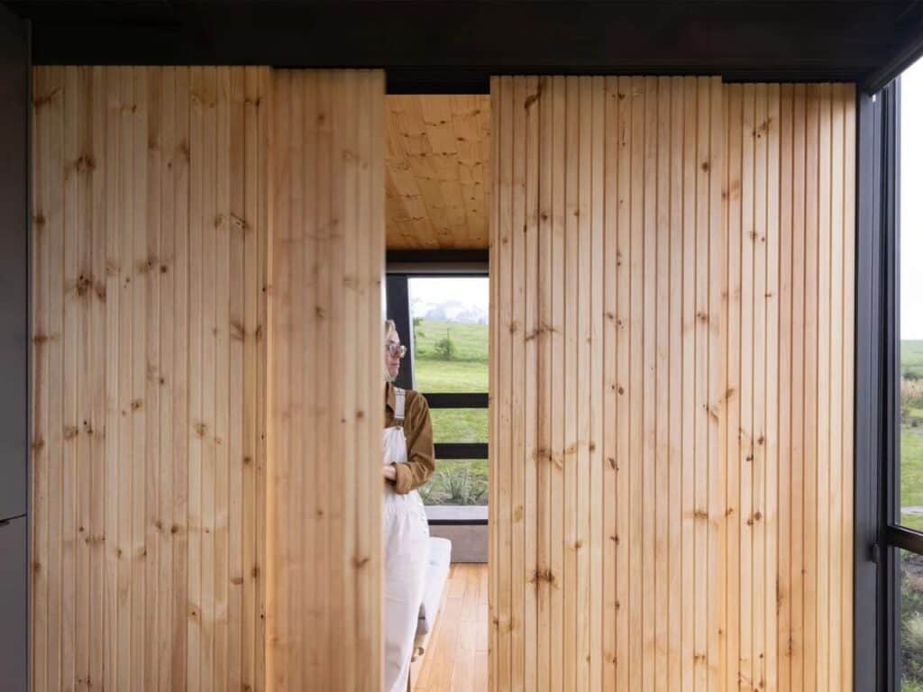 Interior detail of La Miradora showing sliding vertical timber slat doors and a view of the green fields.