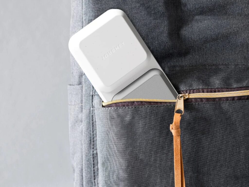 ARIA foldable charging station partially tucked into the pocket of a gray fabric travel backpack.