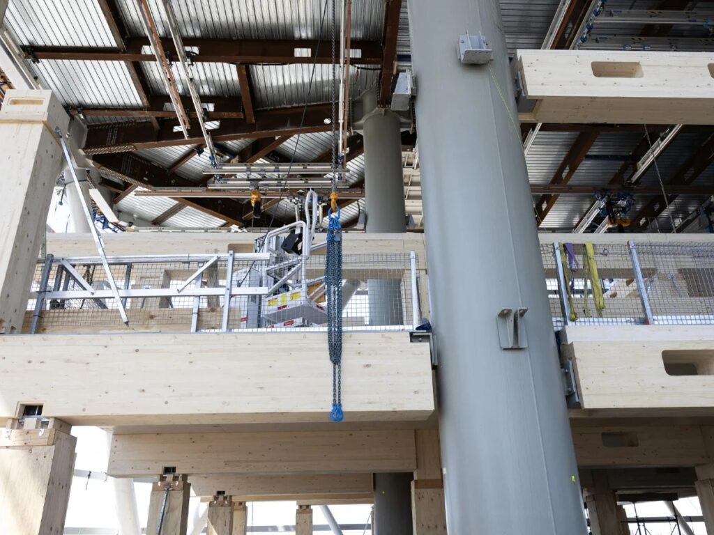 Construction site interior showing a large steel column and mass timber horizontal beams during assembly.
