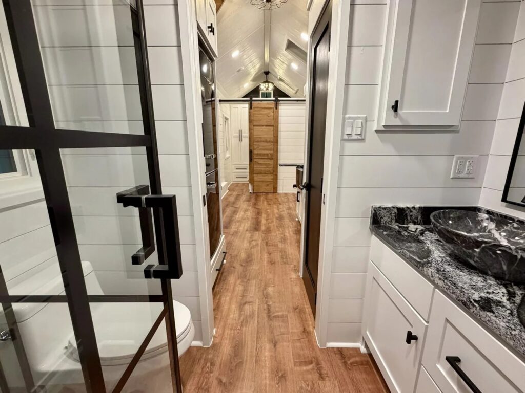 Interior view from the bathroom area looking through the hallway towards the kitchen and bedroom of the tiny house.