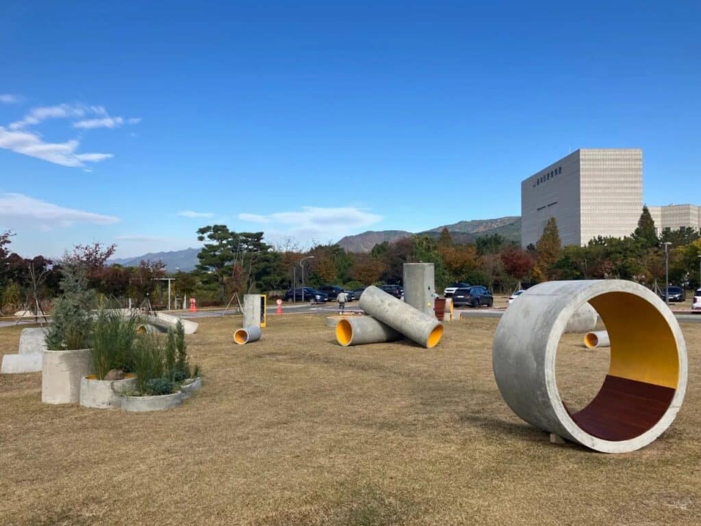Concrete Utopia installation featuring large concrete rings and pipes with the Busan Museum of Contemporary Art building in the background.