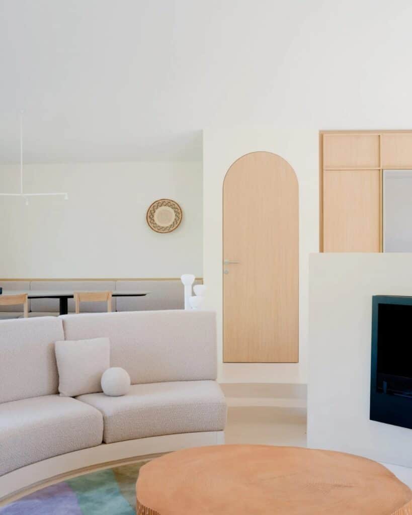 Close-up of a neutral-toned curved sofa and an arched wooden door in the Seaside House minimalist interior.