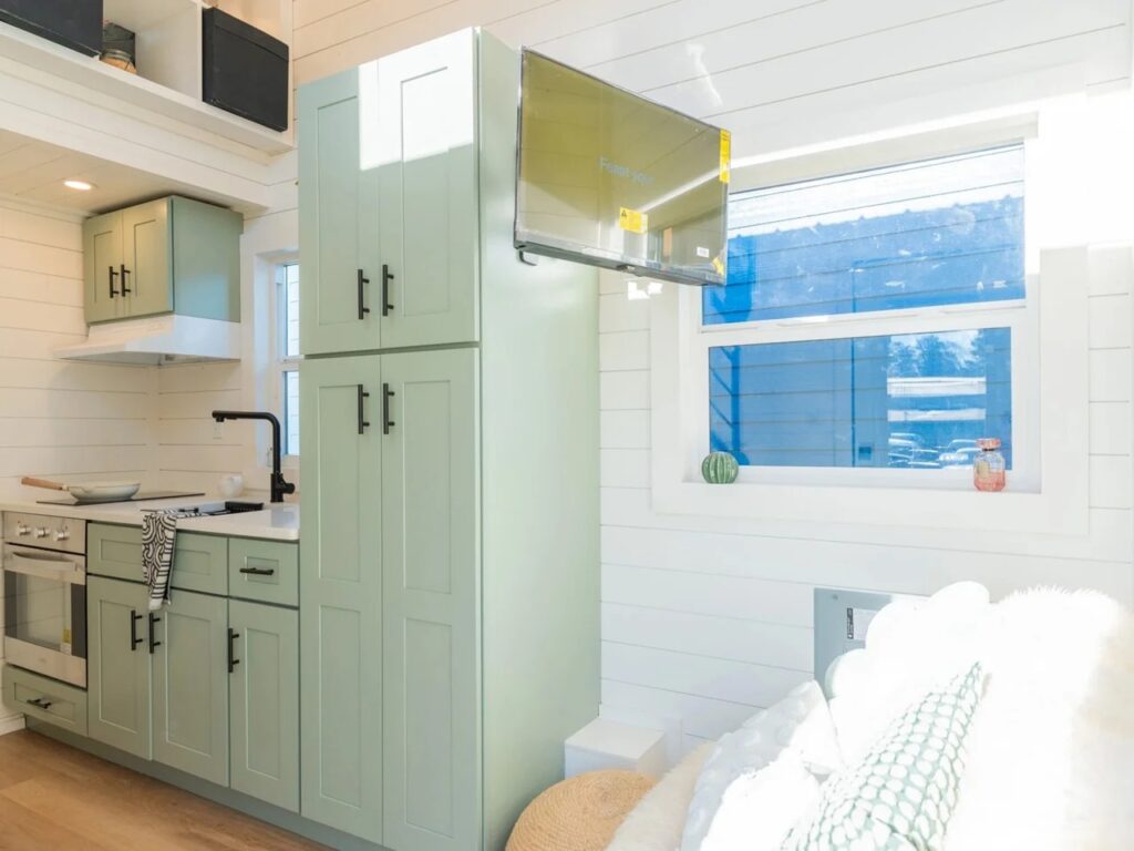 Interior view showing the transition between the living area and the sage green kitchen cabinetry in a tiny home.
