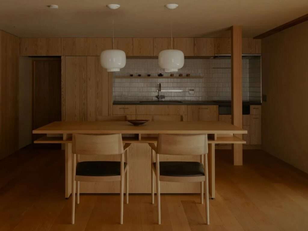 Modern wooden dining table and kitchen area with minimalist white pendant lights in a renovated Kyoto house.