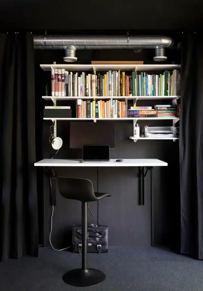 Minimalist home office workspace in Tiny House Shadow with wall-mounted shelves and exposed ventilation pipes.